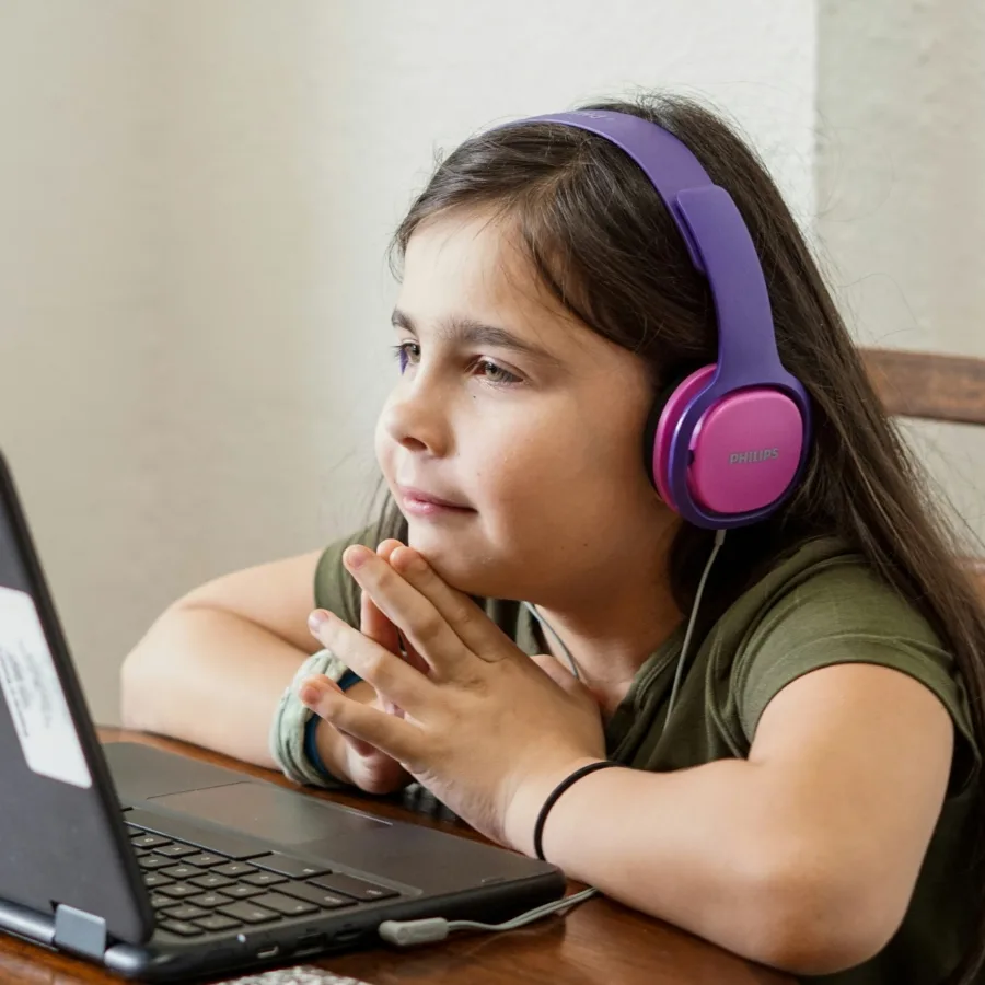 Child listening intently, headphones on, in front of a laptop at home