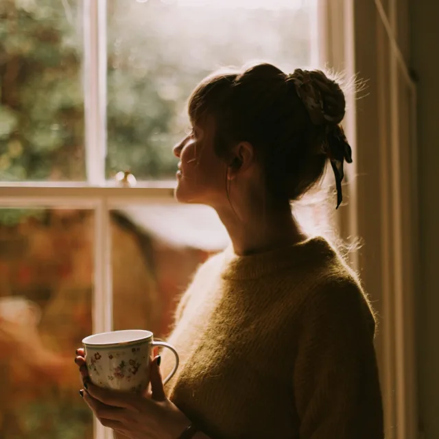 Person holding a mug by a window in the morning light