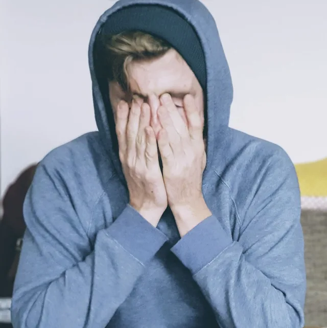 Person in a hoodie, face hidden in their hands