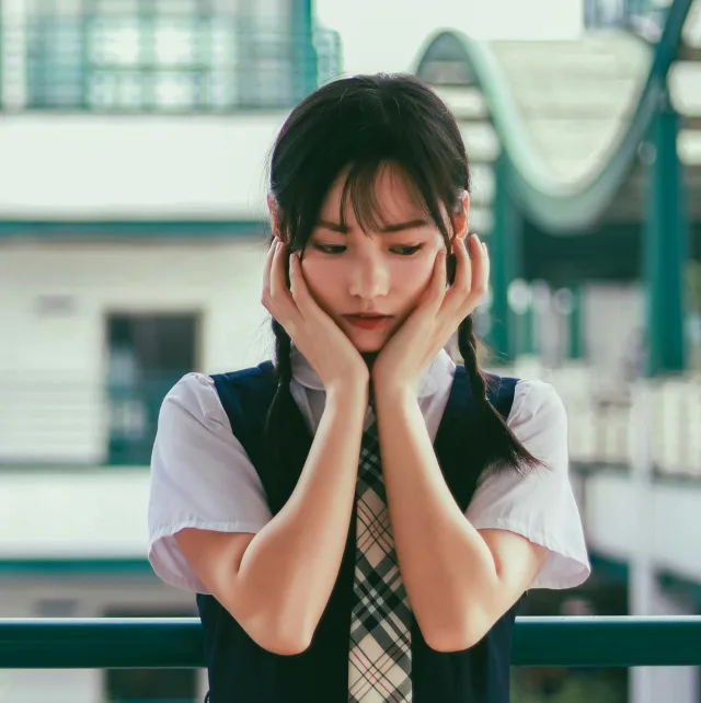 Teenage girl in school uniform, face in her hands, eyes down