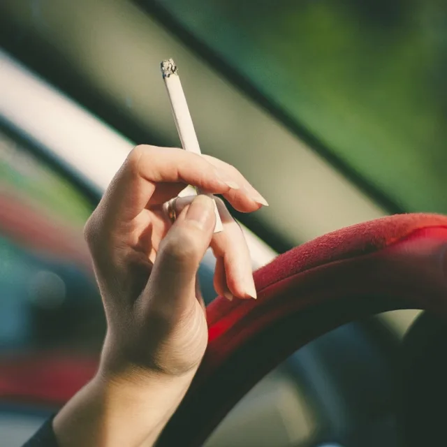 Hand holding a cigarette next to a car steering wheel