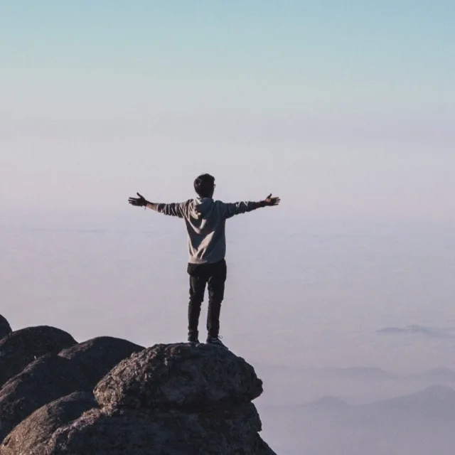 Person with open arms at the top of a mountain, a feeling of freedom