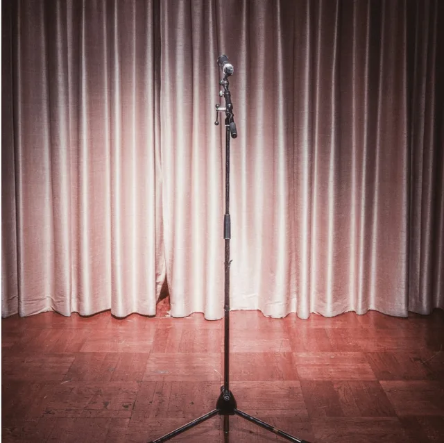 Microphone on a stand, alone on an empty stage in front of a curtain, just before going on