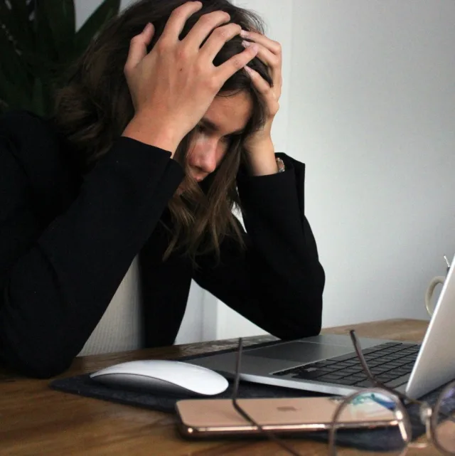Person in a jacket, head in their hands in front of a laptop