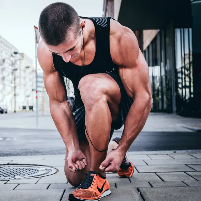 Athlète accroupi, concentré, nouant ses lacets de course juste avant l'effort