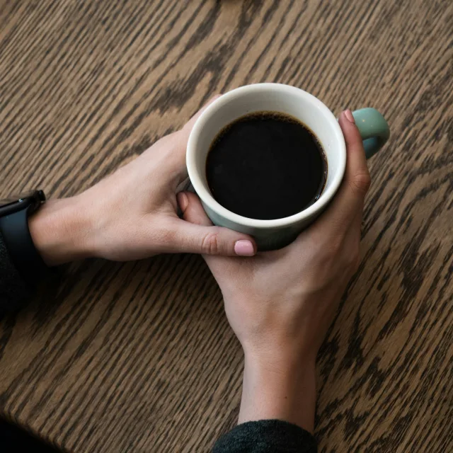 Deux mains refermées autour d'une tasse de café posée sur une table en bois