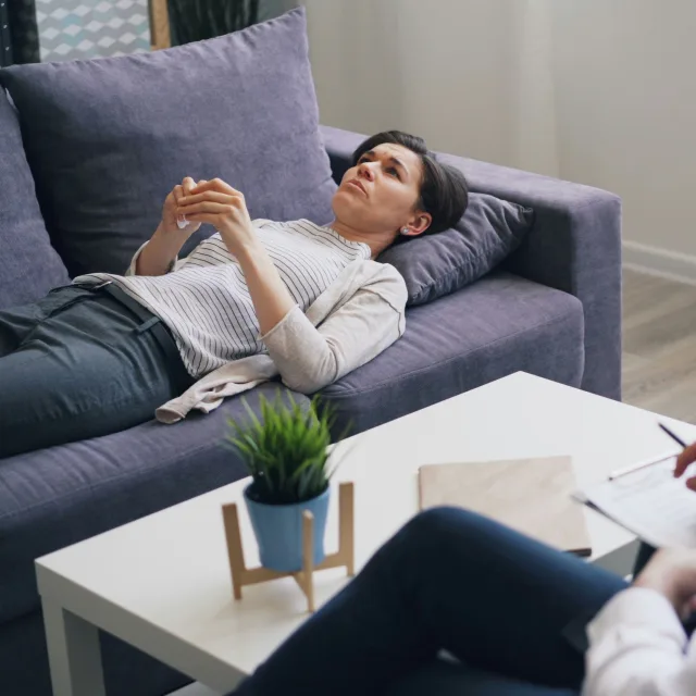 Woman lying on a couch during a session, the practitioner taking notes