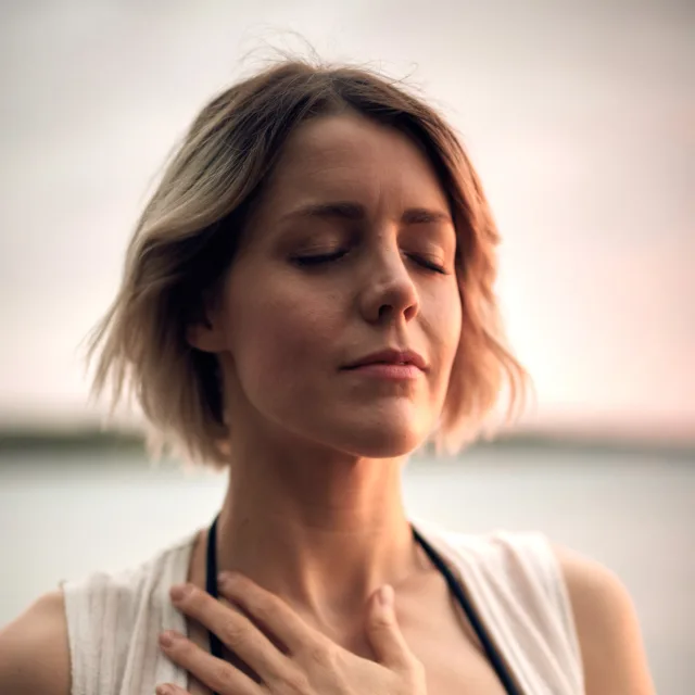 Femme les yeux fermés, une main sur la poitrine, dehors au coucher du soleil