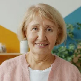 Femme âgée souriante, en cardigan rose, dans une pièce colorée