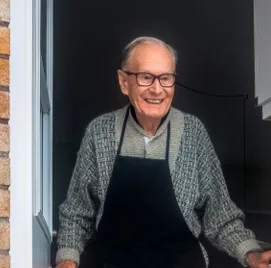 Homme âgé souriant, en tablier, sur le pas de sa porte