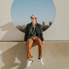Young man sitting on a low wall, in front of a round opening onto the city