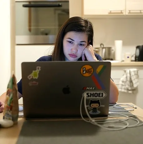 Young woman leaning on her hand in front of her laptop, looking weary