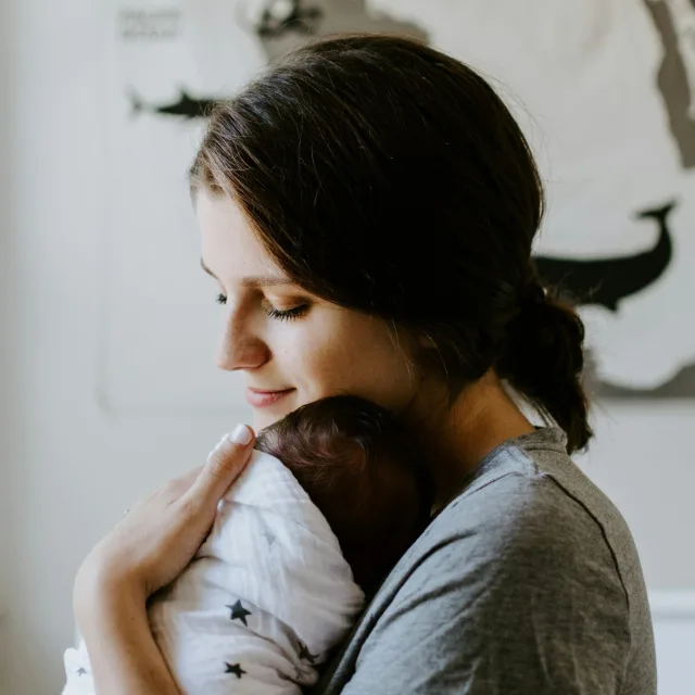 Young mother holding her newborn close to her cheek, eyes closed, smiling peacefully