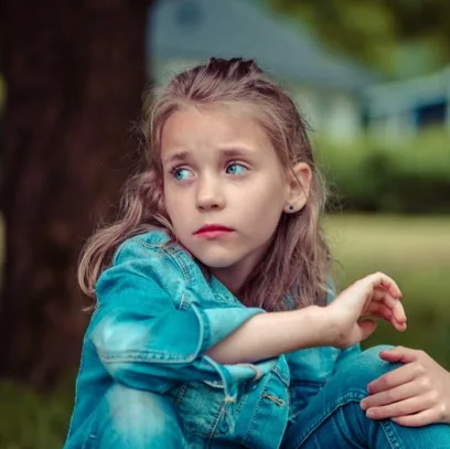 Young girl sitting at the foot of a tree, looking worried