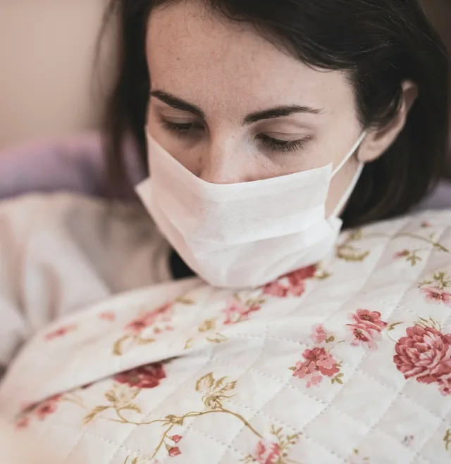Mujer acostada en la cama con mascarilla, la mirada baja